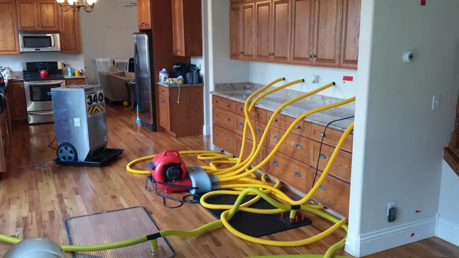Drying mats, yellow hoses, an air mover and a dehumidifier on a wood kitchen floor during a water damage dry-out in Encinitas, CA